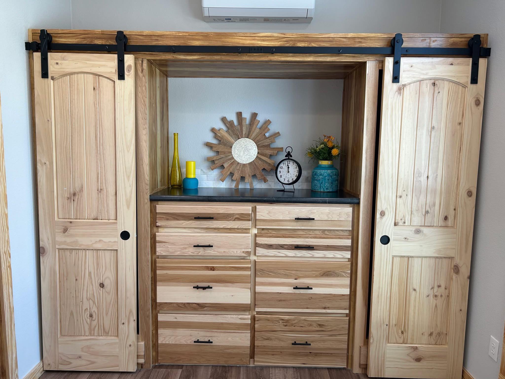 Wooden dresser with sliding barn doors, featuring a sunburst mirror, colorful vases, and a vintage clock. Warm, rustic, and inviting decor.