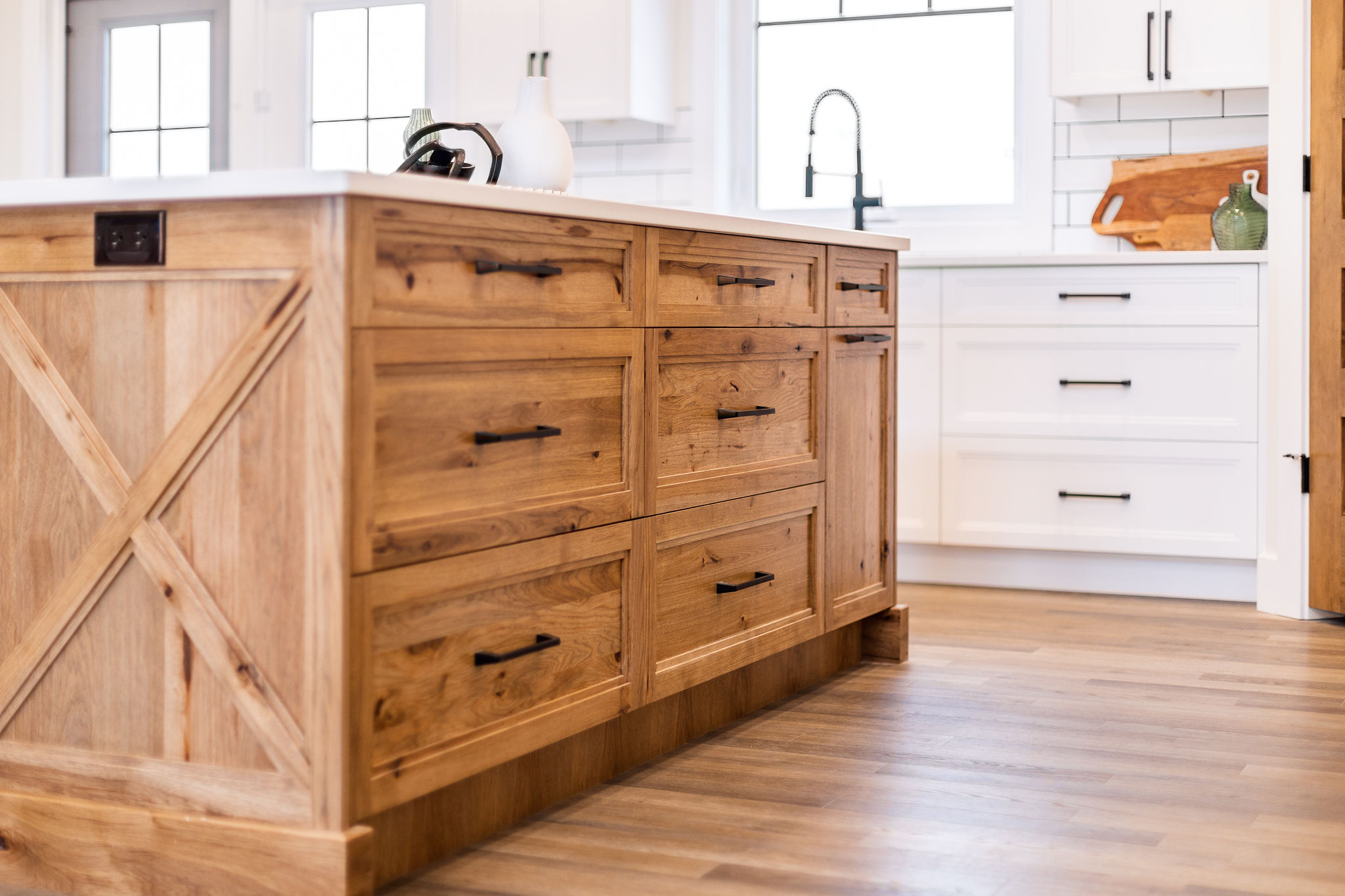 A bright kitchen with a rustic wood island, black handles, white cabinets, and a farmhouse sink. Warm tones and natural light convey a cozy, inviting feel.
