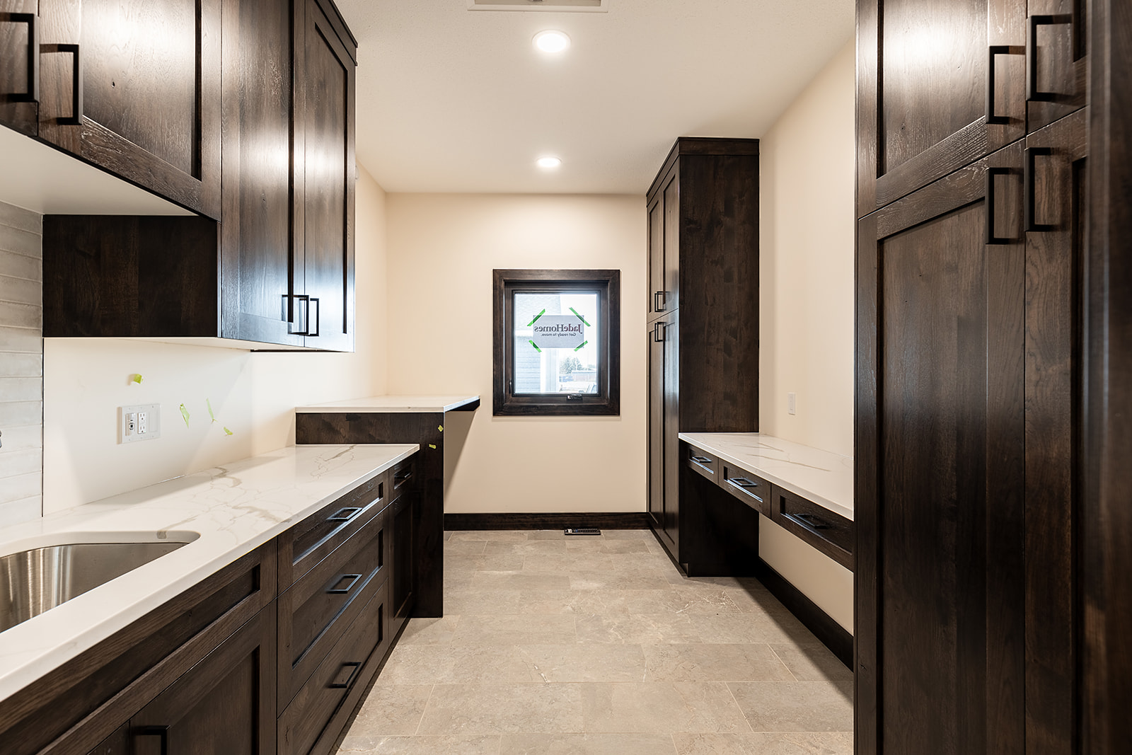 Modern laundry room with dark wood cabinetry, white countertops, and a sleek stainless steel sink. Soft lighting adds warmth to the neutral space.