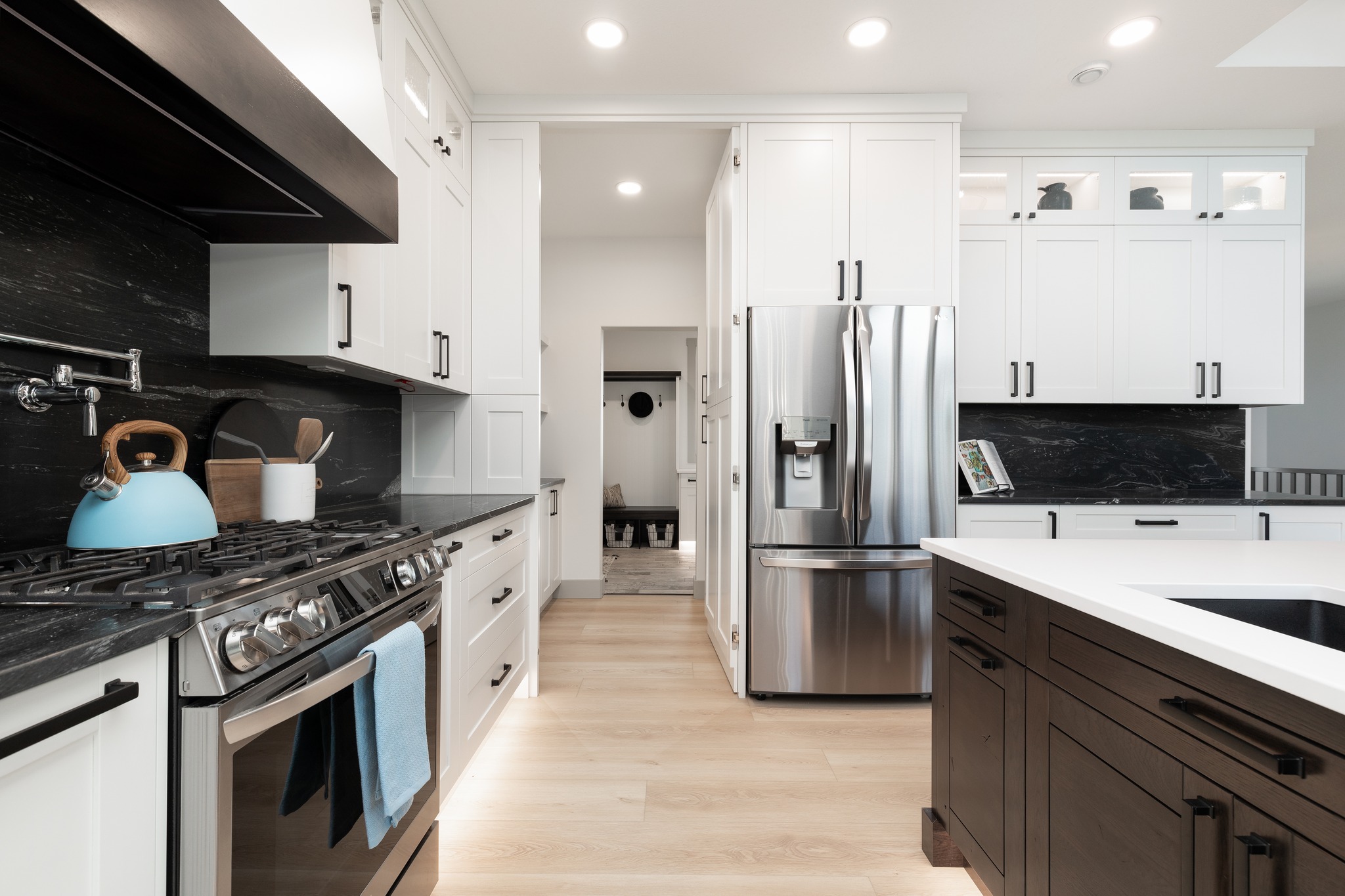 Modern kitchen with black countertops and white cabinets. Stainless steel fridge, stove, and a sky-blue kettle add a sleek, inviting touch.