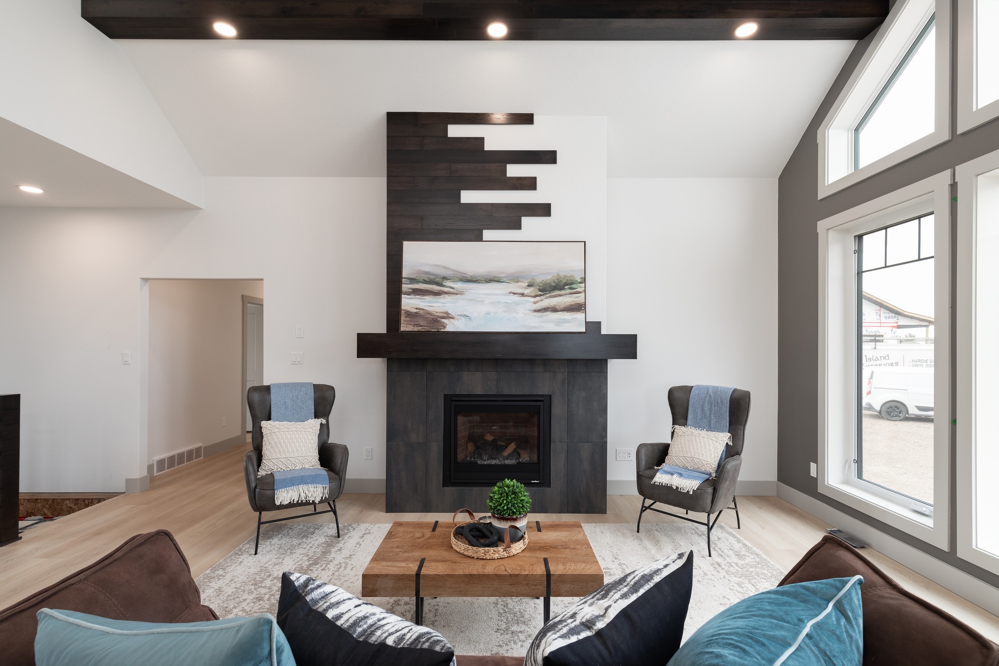 Modern bedroom with gray walls, featuring a dark upholstered bed with blue and white bedding. Three windows provide natural light. Cozy and elegant ambiance.