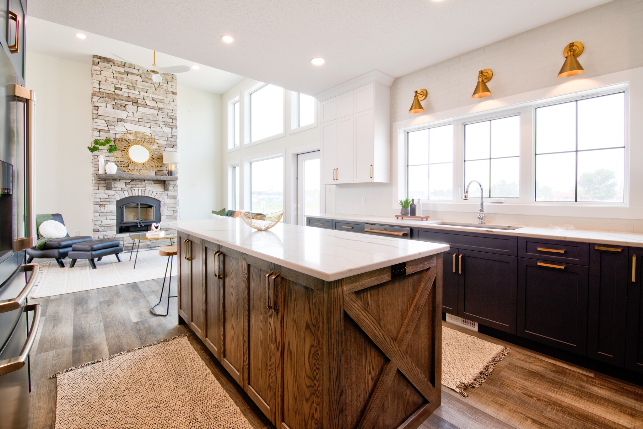 Spacious kitchen with wood island, marble countertop, dark cabinets, and large windows. Adjacent living area features stone fireplace and cozy chairs.