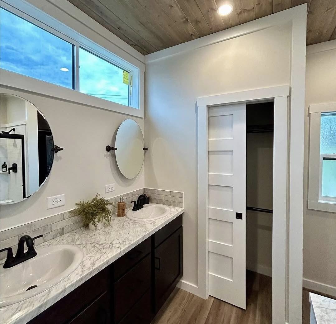 Modern bathroom with dual sinks on a marble countertop, round mirrors above, and black fixtures. A closet with a white sliding door is to the right.