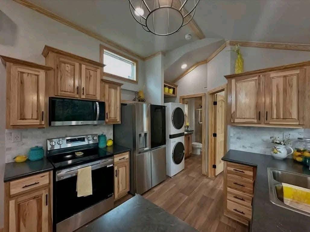 Modern kitchen with natural wood cabinets, stainless steel appliances, and a stacked washer-dryer. Bright and tidy atmosphere with yellow accents.