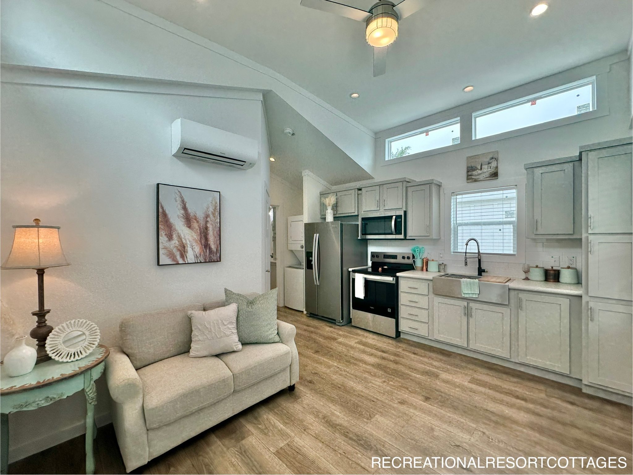 Cozy living area with a beige sofa, a side table with a lamp, and abstract art. Modern kitchen in soft tones, stainless steel appliances, large windows.