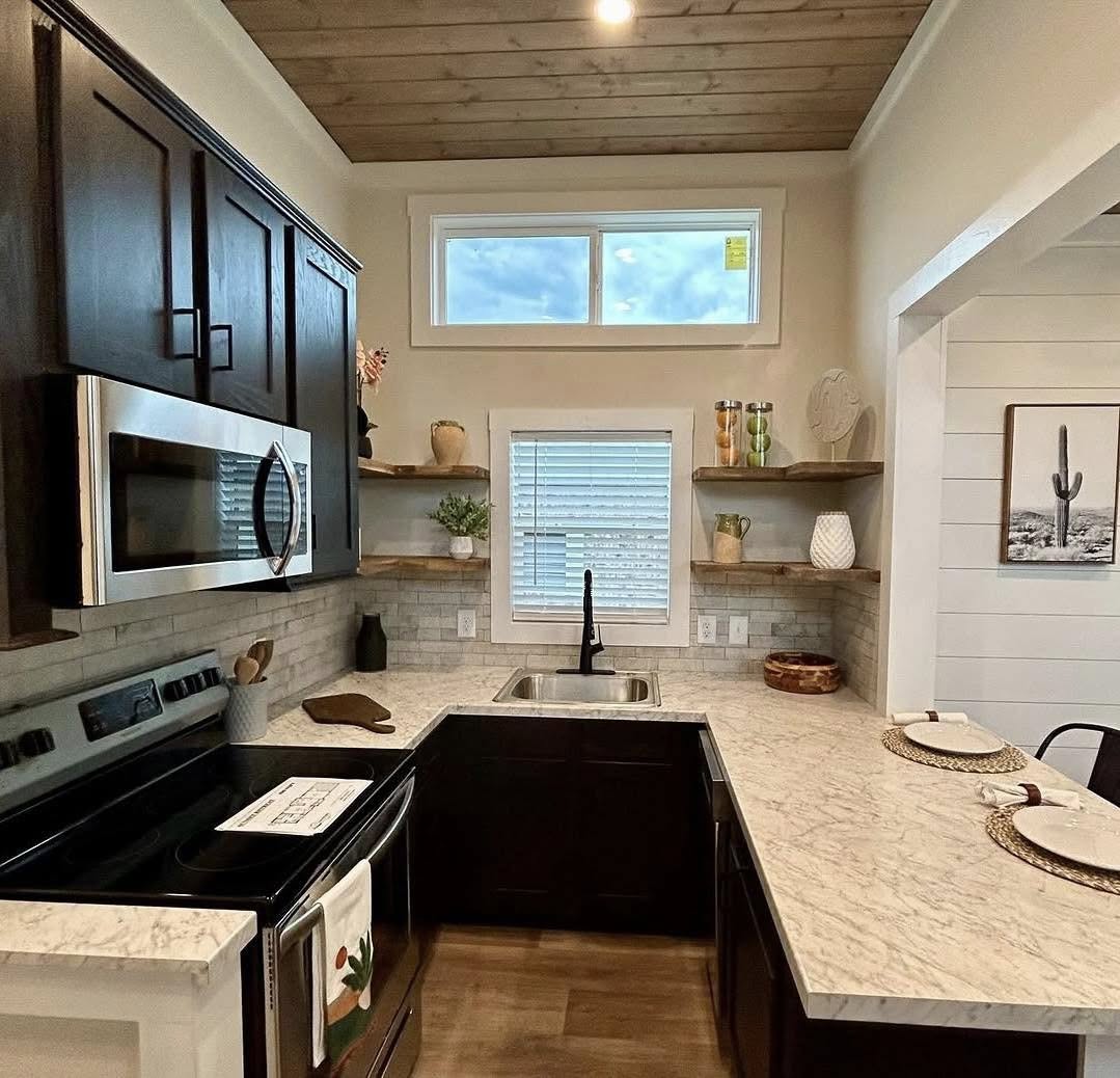 Modern kitchen with dark wood cabinets, stainless steel appliances, and marble countertops. Natural light fills the space from a window above the sink.