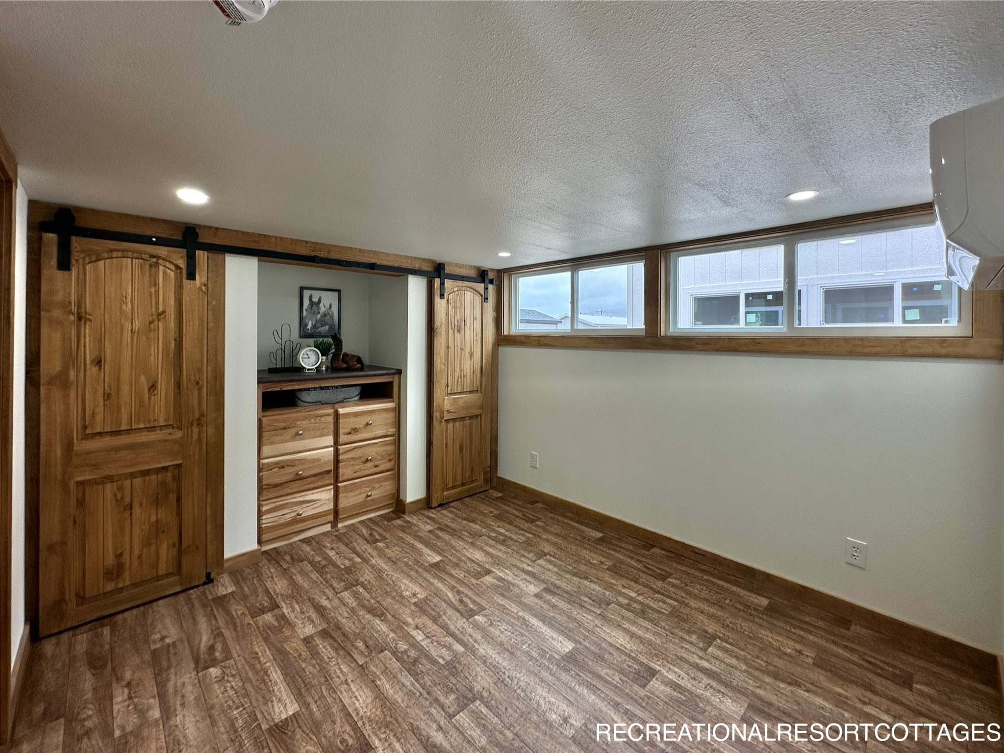 Cozy room with wood flooring, barn doors concealing shelves, and a row of windows allowing natural light. Warm, rustic ambiance with recessed lighting.