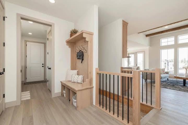 Bright, modern entryway with light wood flooring, a bench with cushions, black hooks for hanging items, and stairs leading to a sunlit living room.