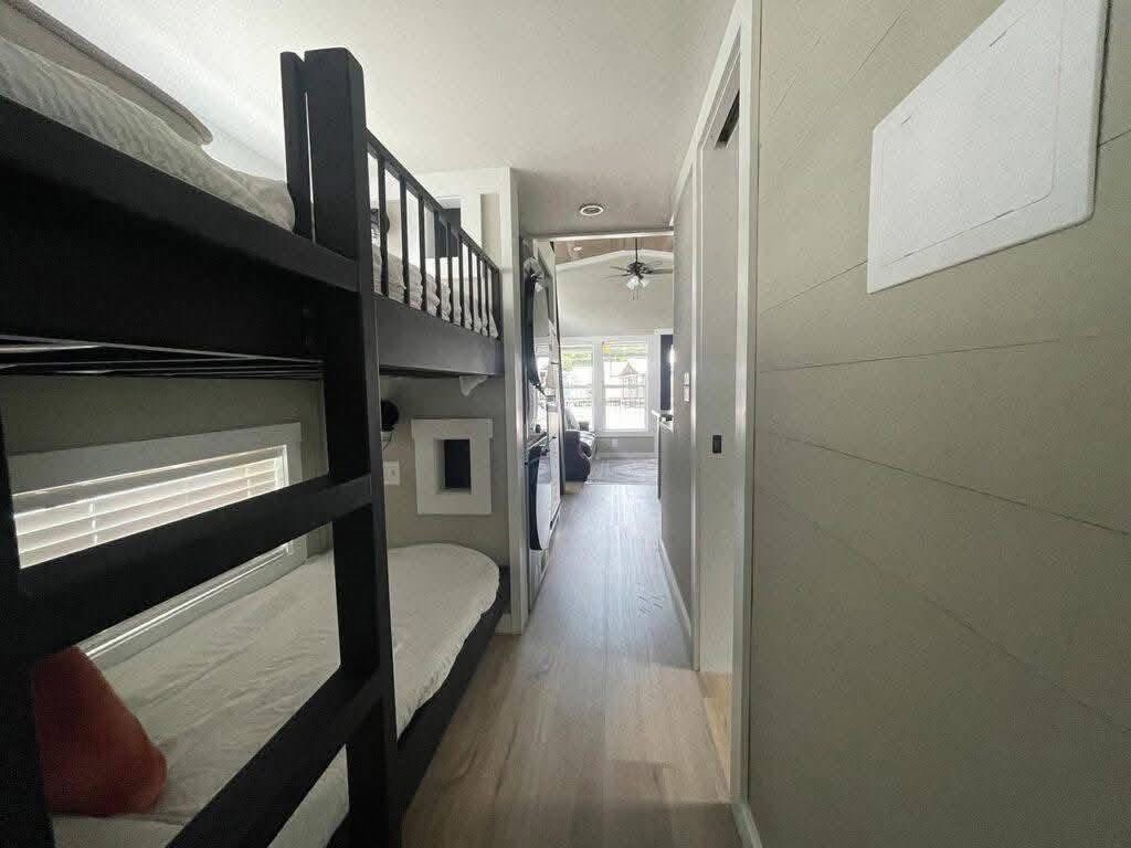Cozy interior of a narrow room with dark wooden bunk beds on the left and a small hallway leading to a bright living area with a ceiling fan.