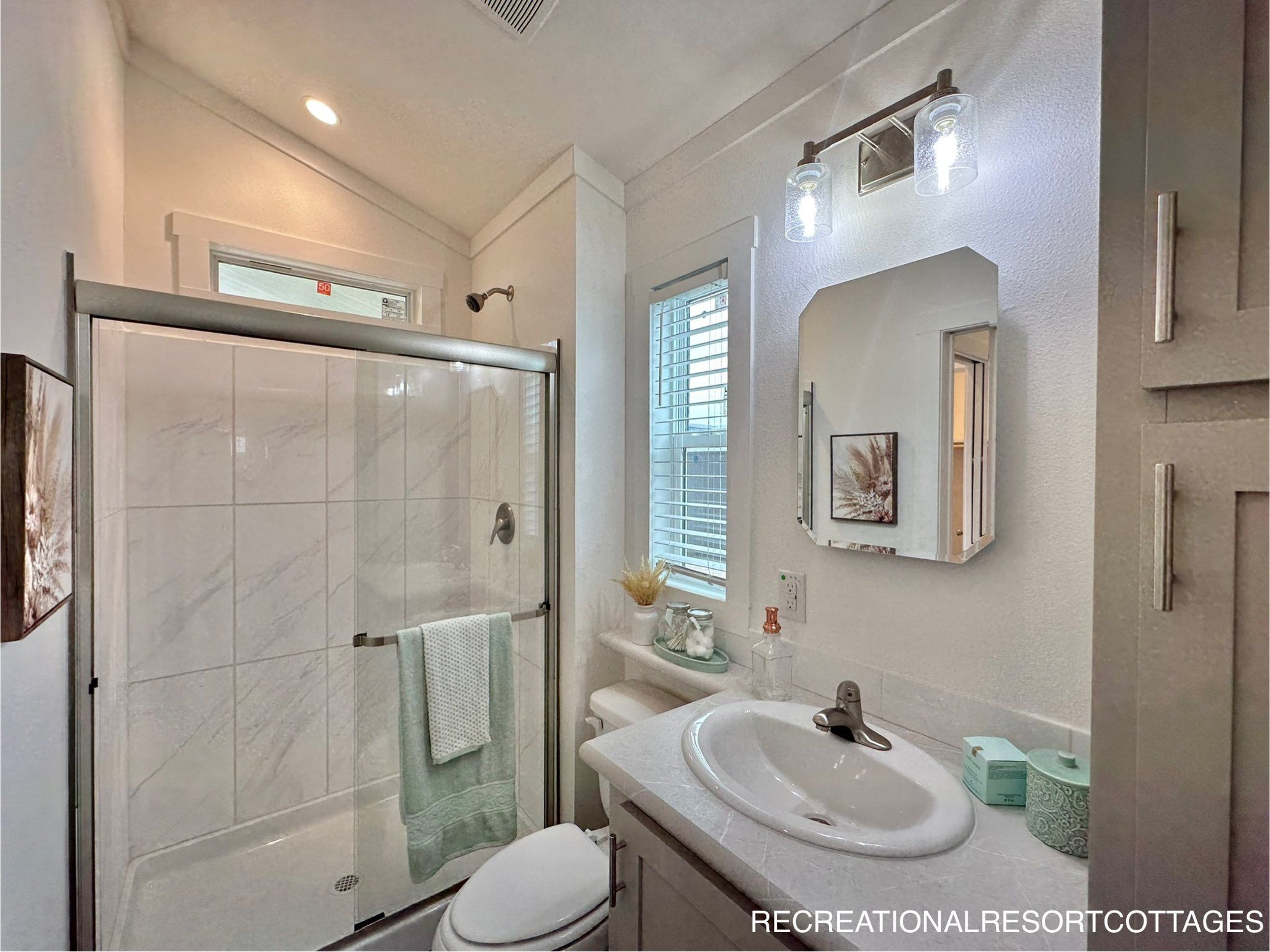 Bright, modern bathroom with a glass-enclosed shower, white tiles, and mint green towel. Vanity with a rectangular mirror and soft lighting.