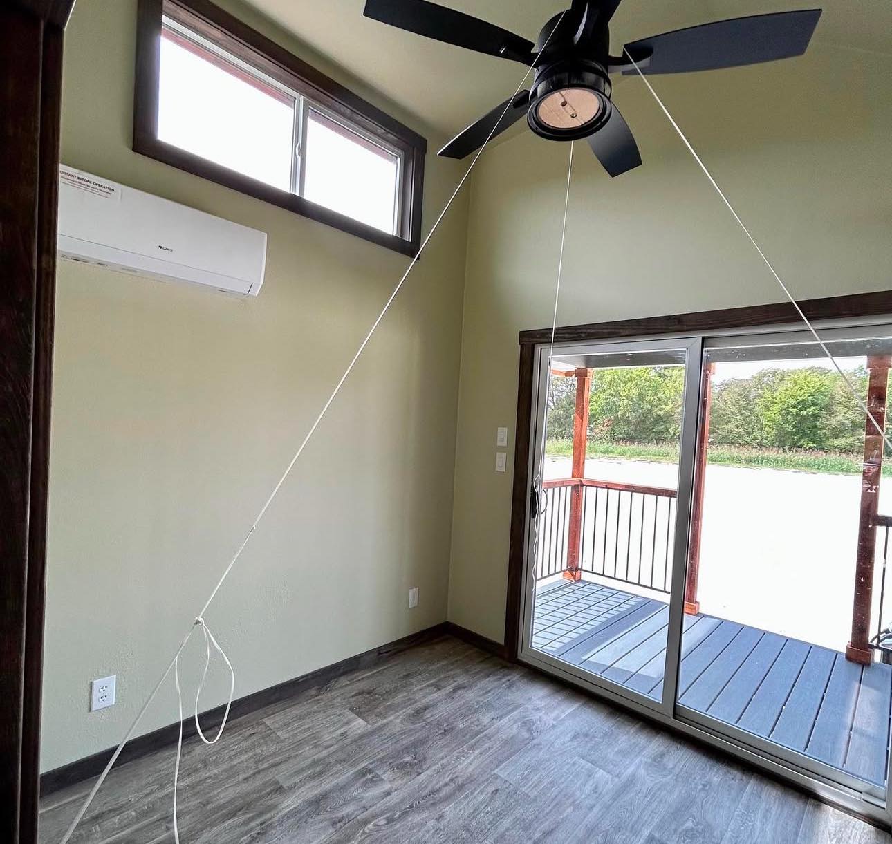 Minimalist room with sliding glass doors leading to a porch. Ceiling fan and air conditioner above. Bright, natural light and tranquil outdoors.