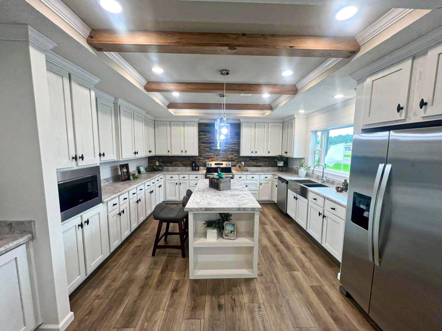 Modern kitchen with white cabinets, marble island, and wood beams. Stainless steel appliances, wood flooring, and warm lighting create a cozy ambiance.