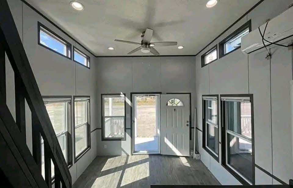 Spacious room with high ceiling, large windows filling the space with light. A ceiling fan is centered, with gray walls and dark trim for contrast.