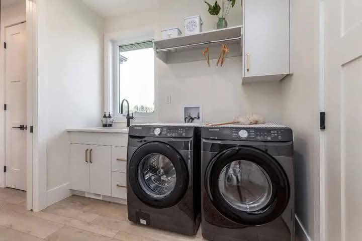 Modern laundry room with sleek black washer and dryer, light cabinets, a small window, and a shelf with decor, exuding a clean, minimalist vibe.