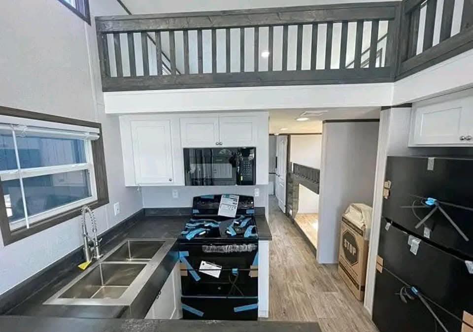 Modern kitchen interior featuring white cabinets, a black oven with blue protective tape, double sink, and large loft area above. Bright and spacious.