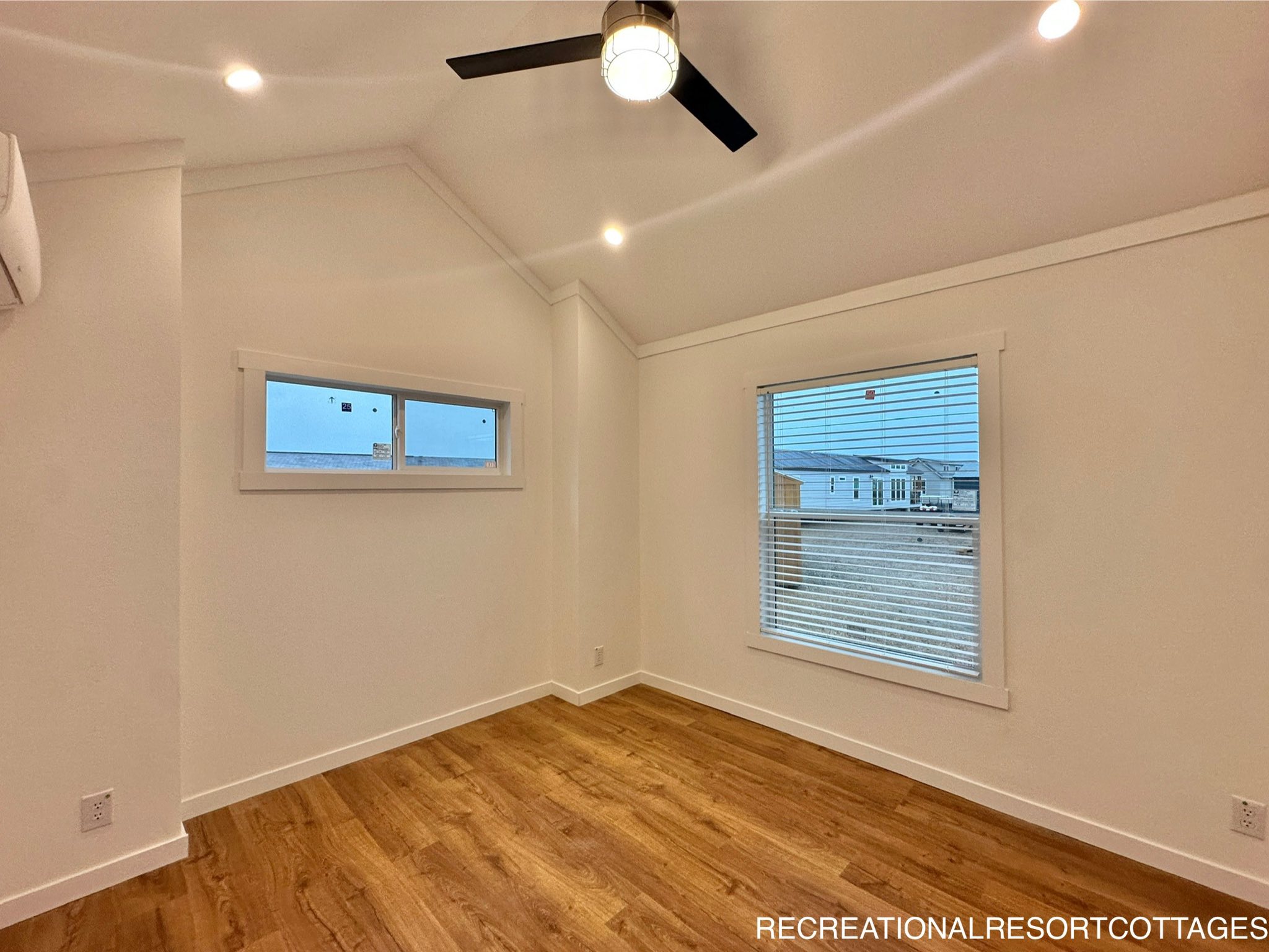 Minimalist room with wooden floors, white walls, and high ceiling. Features a modern ceiling fan, rectangular windows, and a calm, spacious atmosphere.