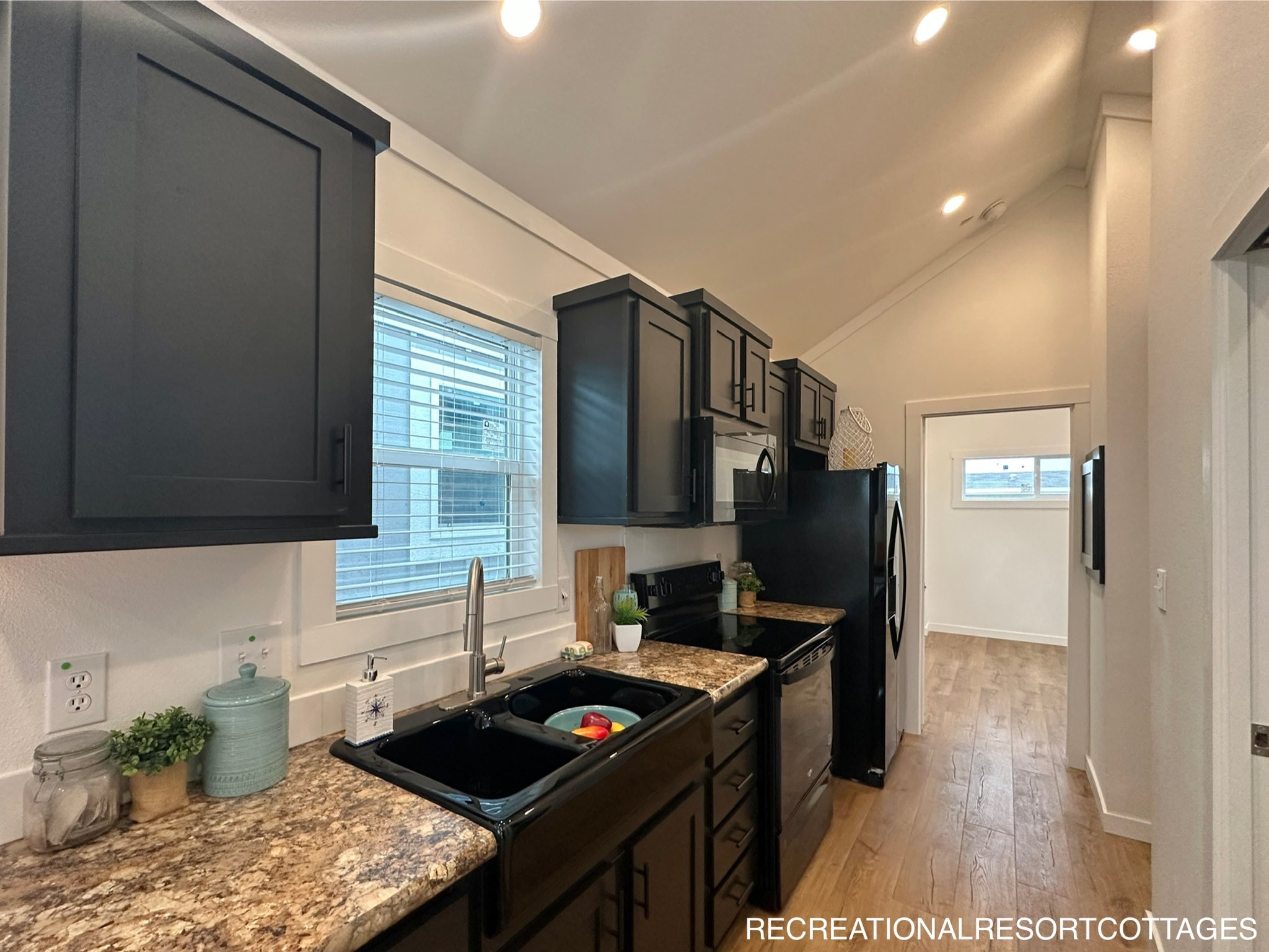 Modern kitchen with dark cabinets and marble countertops. Includes a black sink, stainless steel appliances, and wooden floor. Bright and spacious.