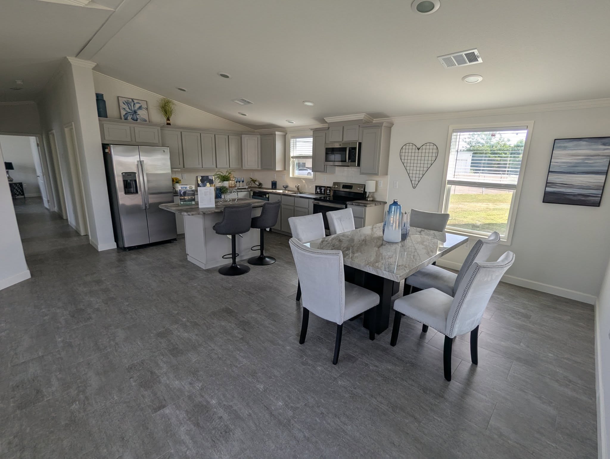 Modern open-plan kitchen and dining area with light gray cabinetry, stainless steel appliances, a marble table, and light gray upholstered chairs.