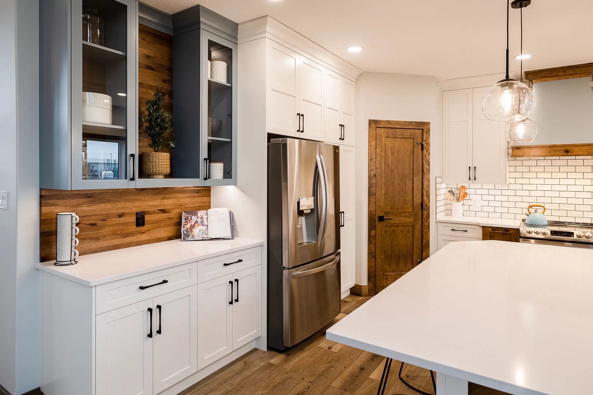 Modern kitchen with white cabinets, stainless steel appliances, and wooden accents. Bright, tidy, and welcoming space with pendant lights over an island.