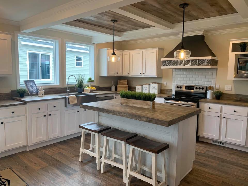 Rustic kitchen with white cabinets, wooden countertops, and an island with stools. Pendant lights hang from a coffered ceiling, adding warmth.