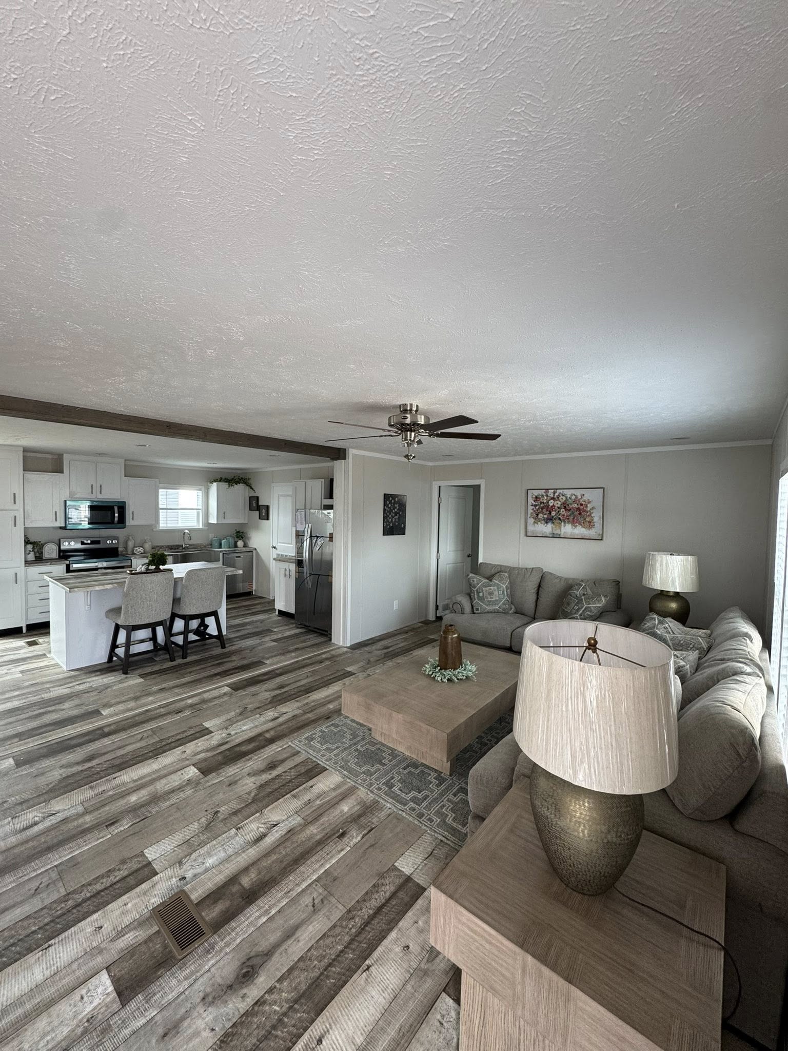 A modern open-plan living room and kitchen with wood flooring. The room has a neutral-toned sofa, a wooden coffee table, and light fixtures, conveying a cozy and inviting atmosphere.