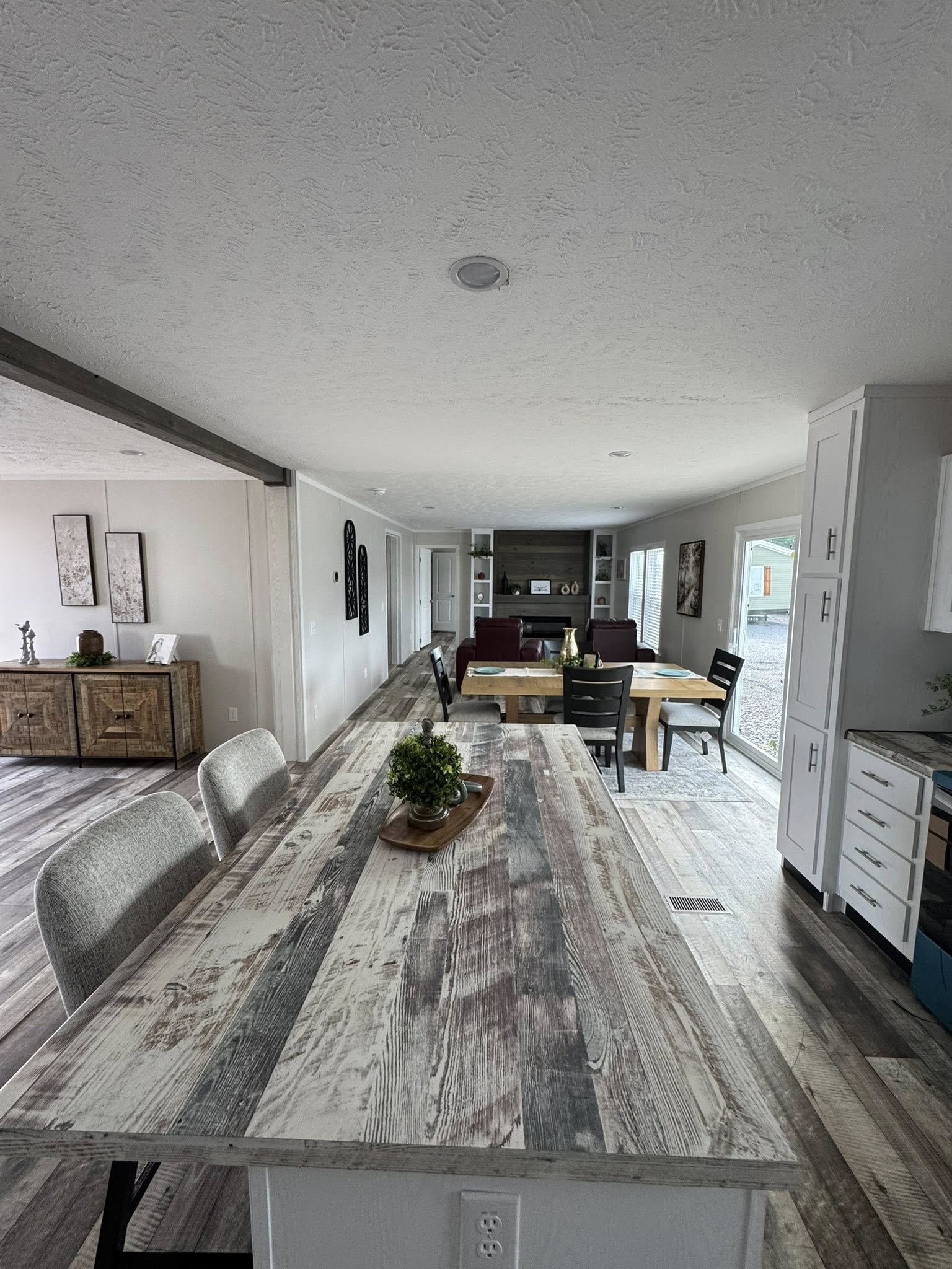 Wide angle view of an open-plan living space featuring a rustic wooden dining table, cushioned chairs, and a cozy living area with a sofa and decor.