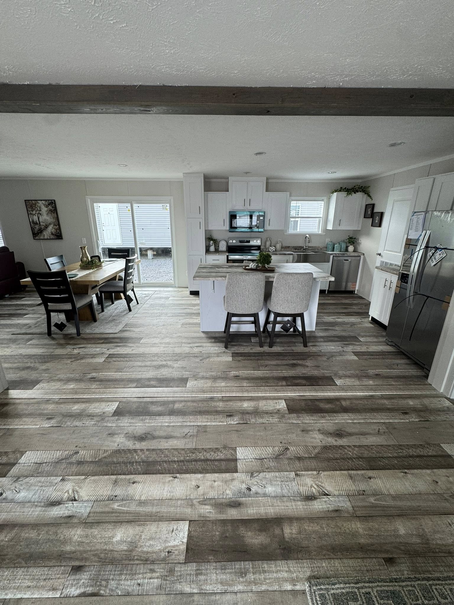 Modern kitchen and dining space with white cabinetry, a central island with two chairs, stainless steel appliances, wooden flooring, and natural light.