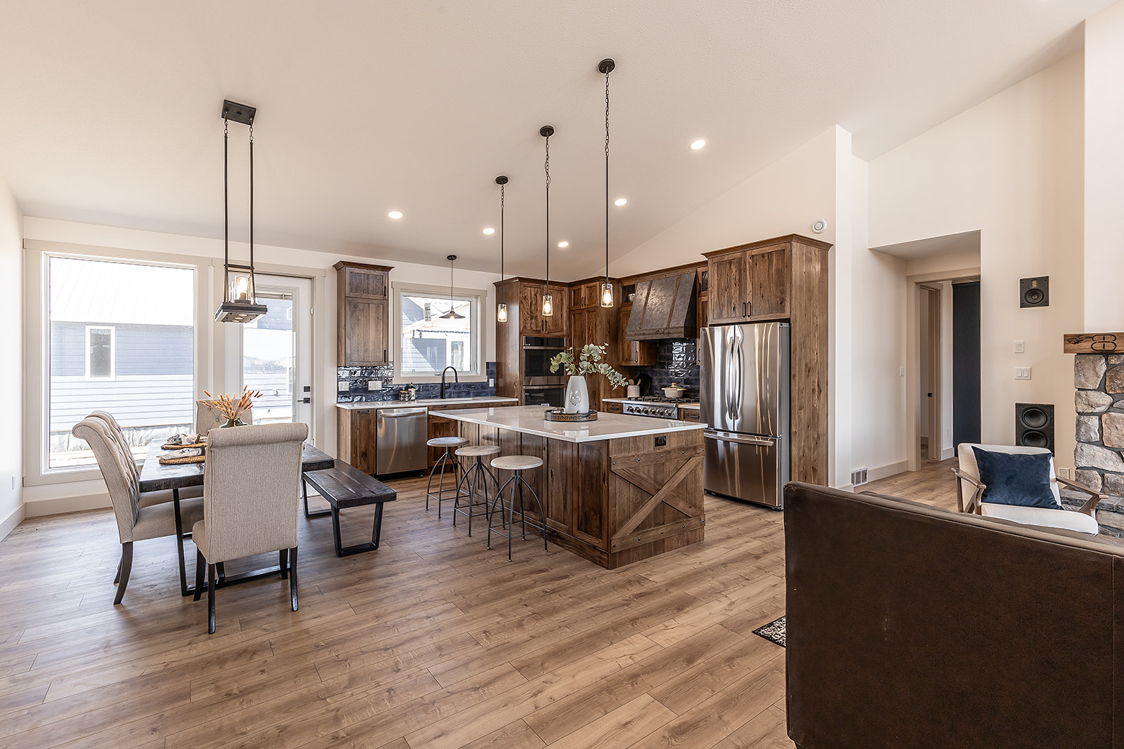 A spacious kitchen and dining area with rustic wood cabinets, a large island, pendant lights, and a cozy stone fireplace. Warm tones create a welcoming atmosphere.