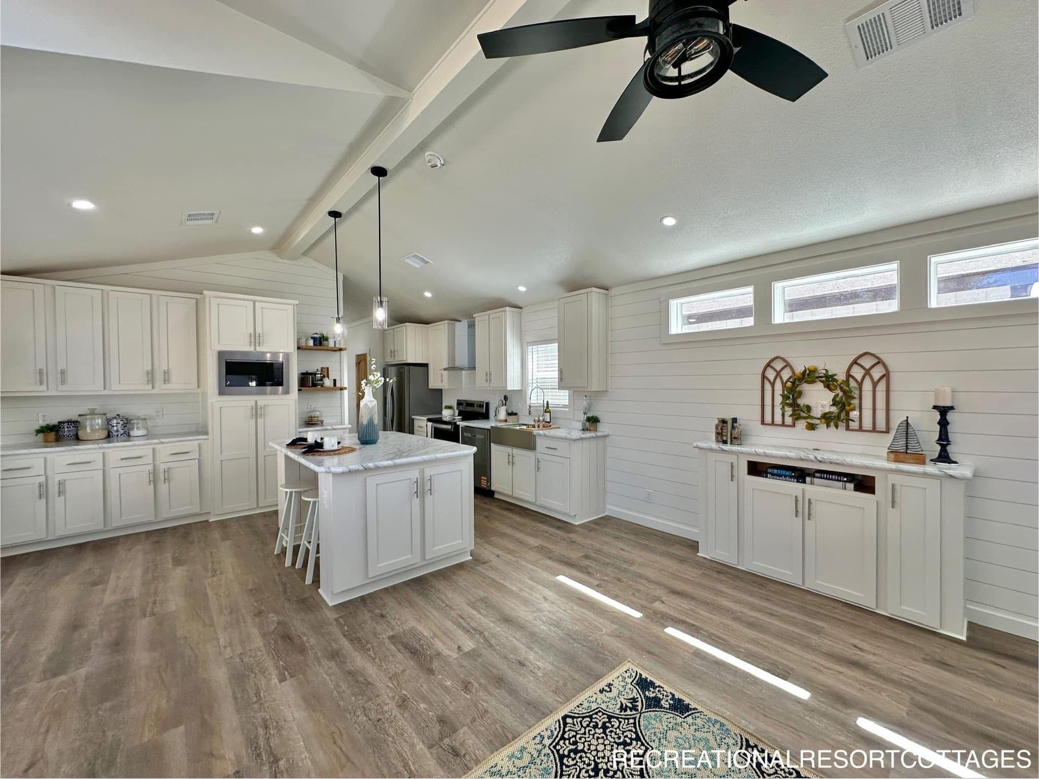 Spacious kitchen with white cabinets, marble island, and stainless steel appliances. Shiplap walls, ceiling fan, and natural light create an airy feel.