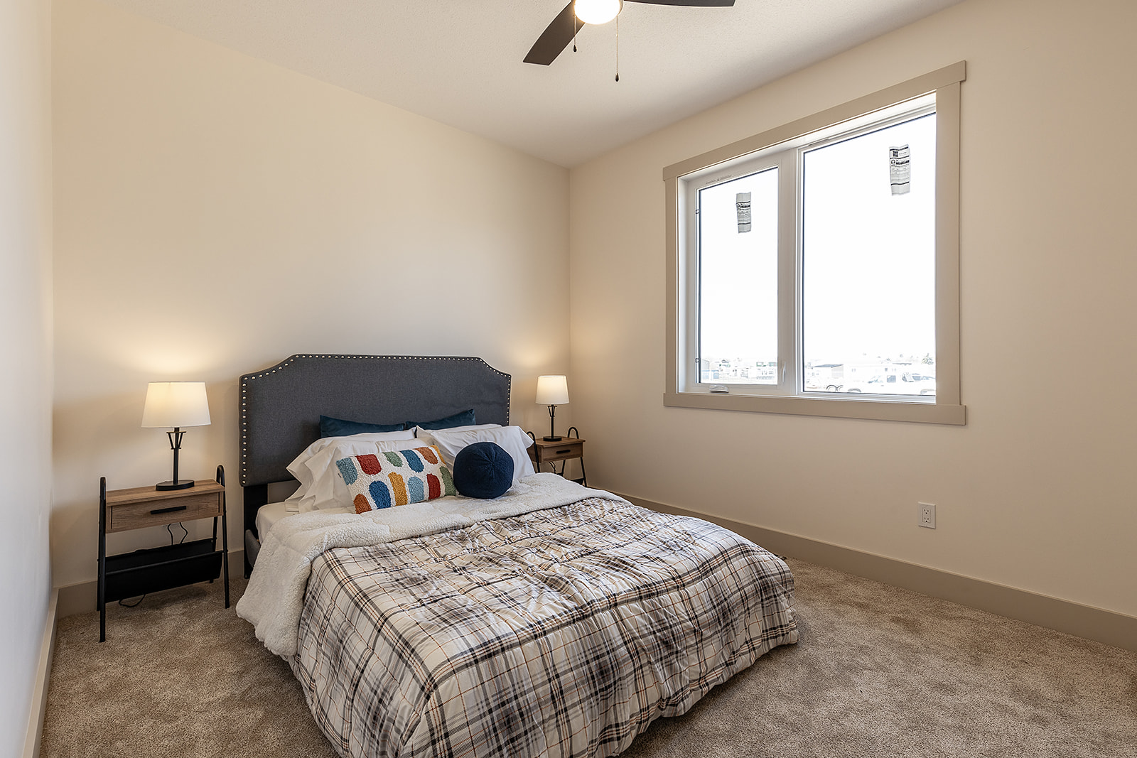 A cozy bedroom with a neatly made bed featuring plaid bedding and colorful pillows. Soft lighting from two bedside lamps creates a warm atmosphere.