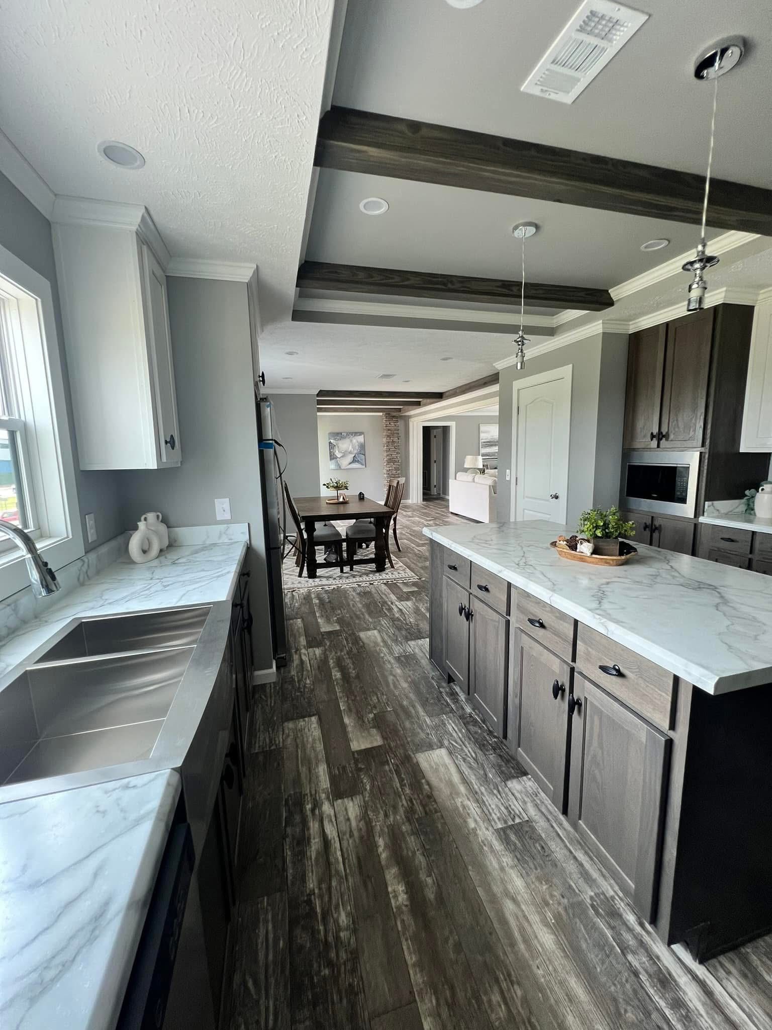 Modern kitchen with gray cabinets, marble countertops, and wood flooring, leading to a dining area with a table. Bright, airy, and elegant atmosphere.