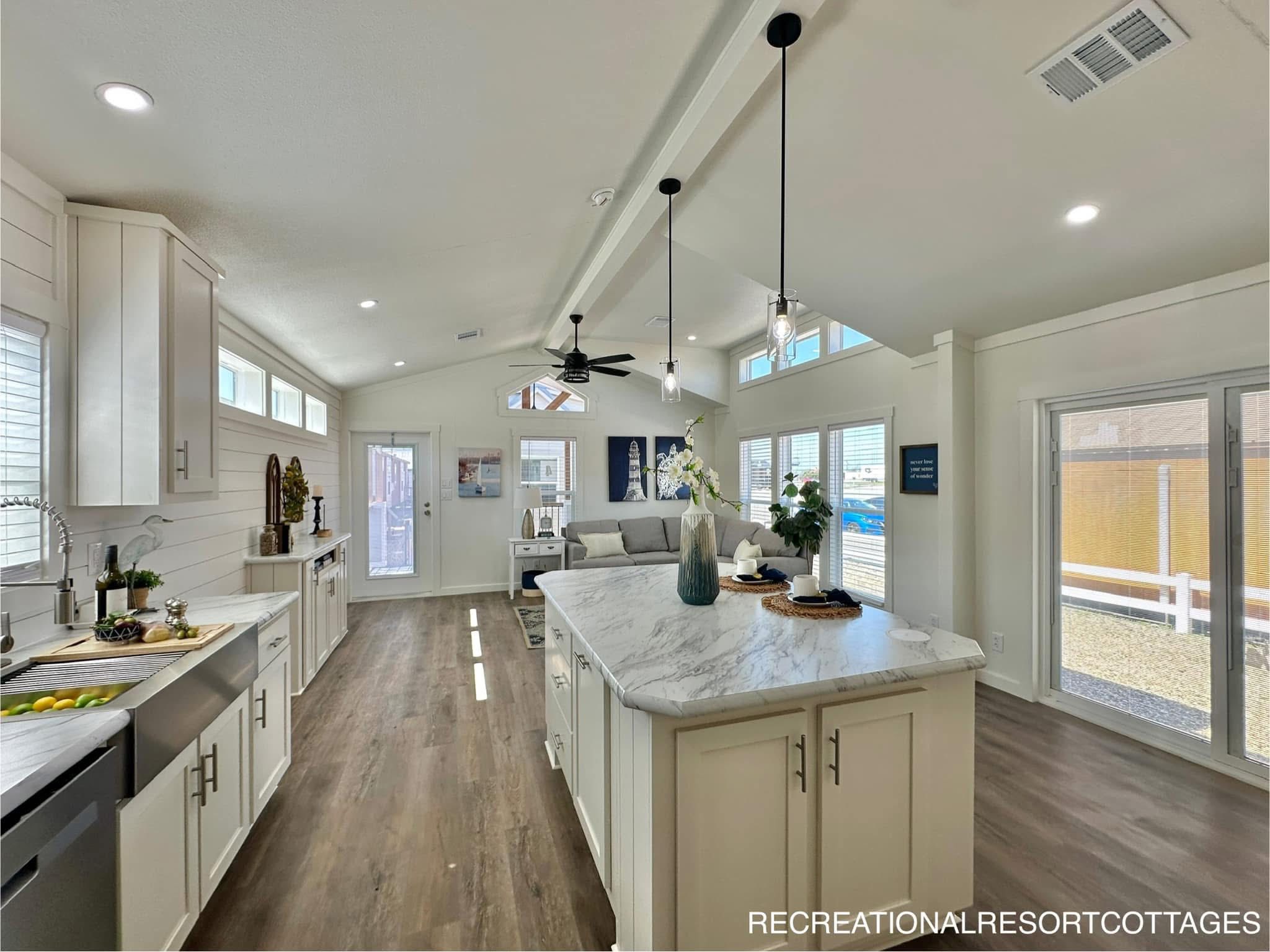 Spacious, bright kitchen and living area with white cabinets, marble island, pendant lights, and a cozy sofa. Wood flooring adds warmth and elegance.