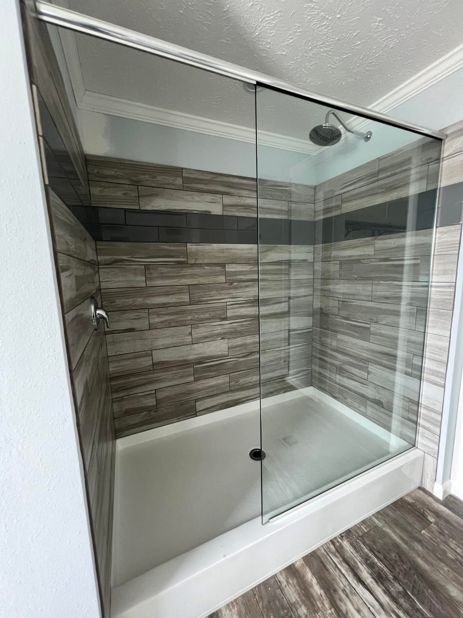Modern shower with a glass door, wood-textured tiles in shades of gray. The sleek design conveys a clean and contemporary feel.