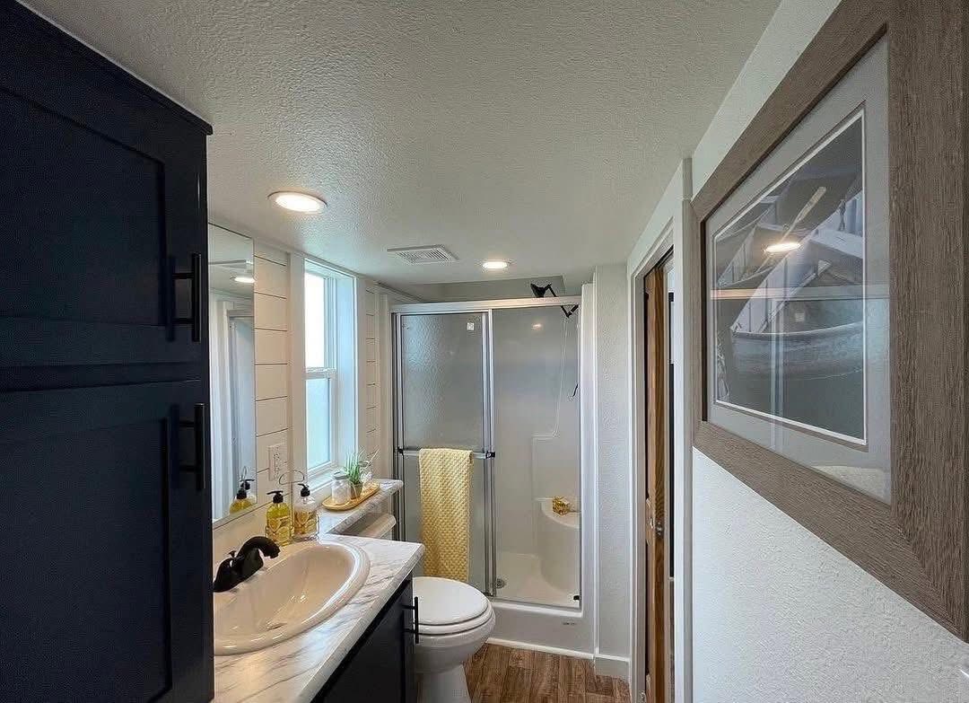 Modern bathroom with a glass shower, white sink, and wooden cabinets. A yellow towel hangs, adding a bright touch. A framed picture on the wall.