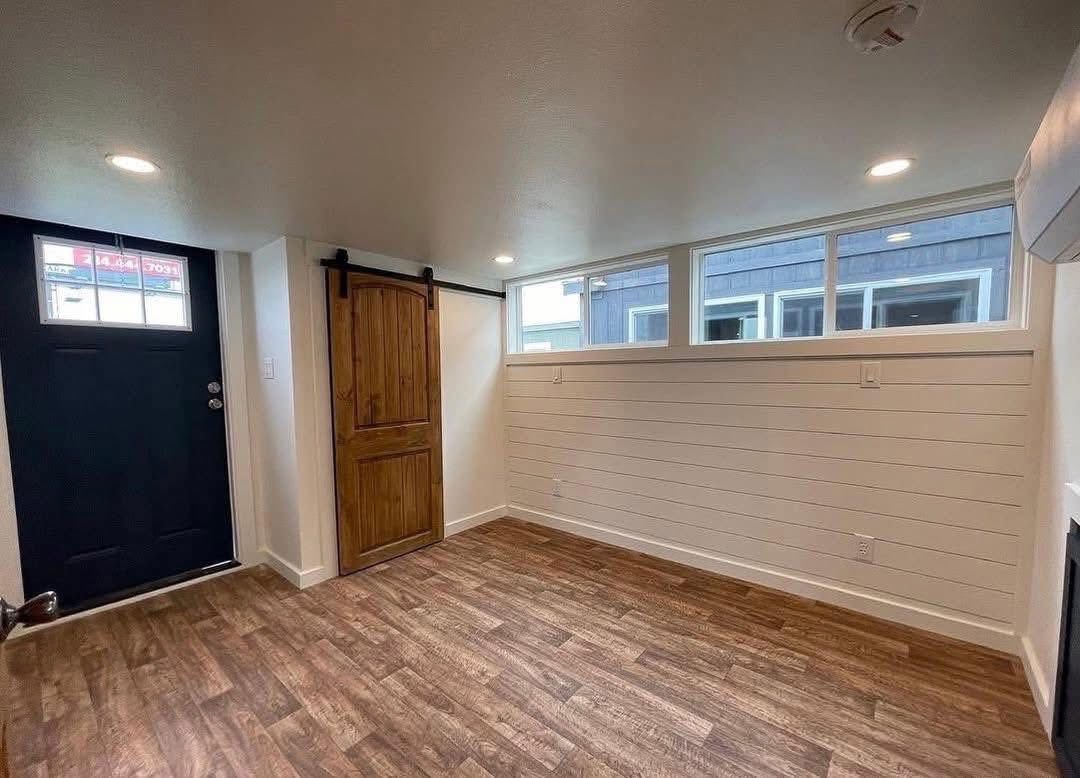 A small, cozy room with wood flooring, a black door, and a wooden sliding barn door. White shiplap walls create a warm, modern ambiance.