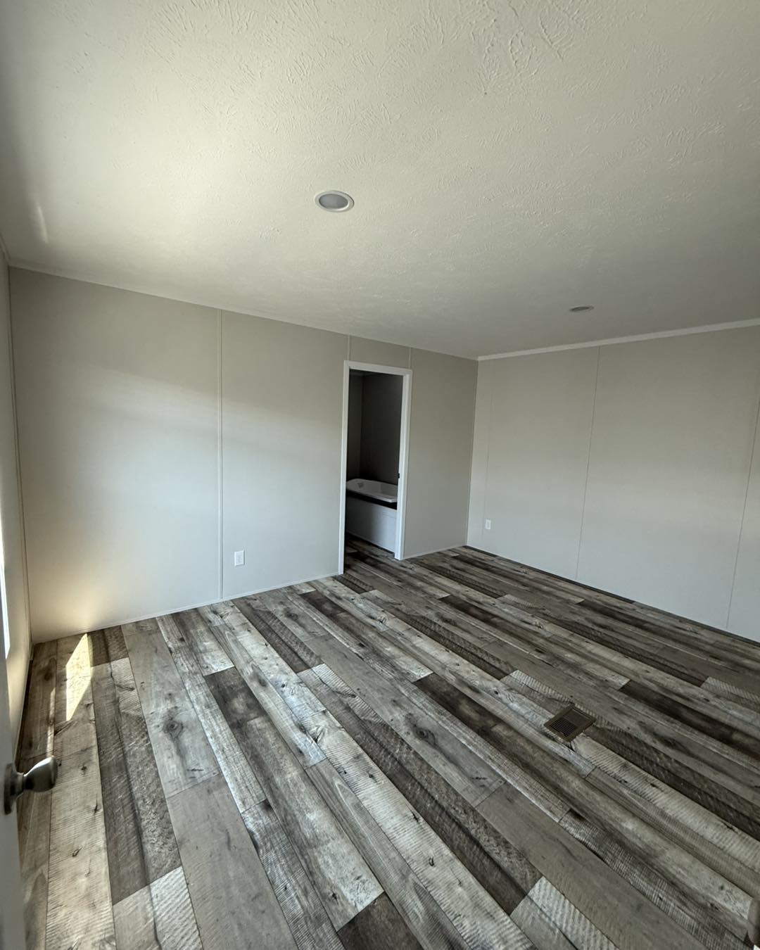 Narrow hallway with white walls and a white door at the end. Wood-textured floor and a small closet with a single wire shelf on the right.