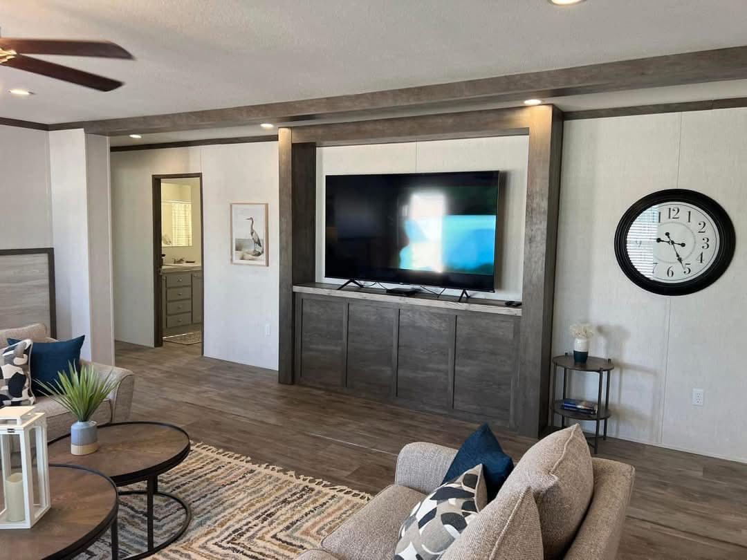 Modern living room with a large flat-screen TV mounted on a wooden entertainment center. A round clock hangs on the wall. Neutral tones create a cozy atmosphere.