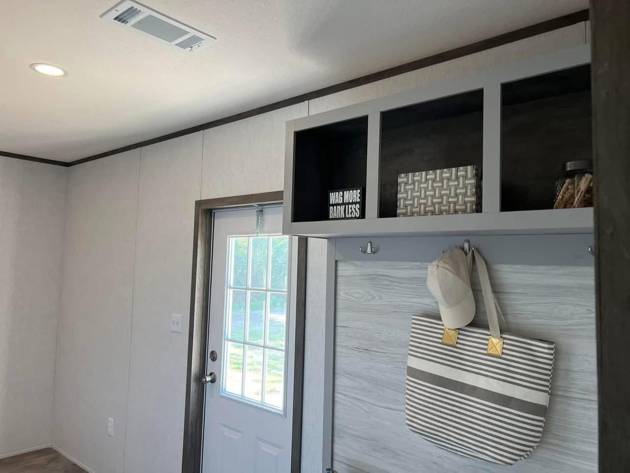 A home entryway with a door featuring glass panes. A shelf holds a decorative basket and a "Wag More Bark Less" sign, while a striped bag and cap hang below.