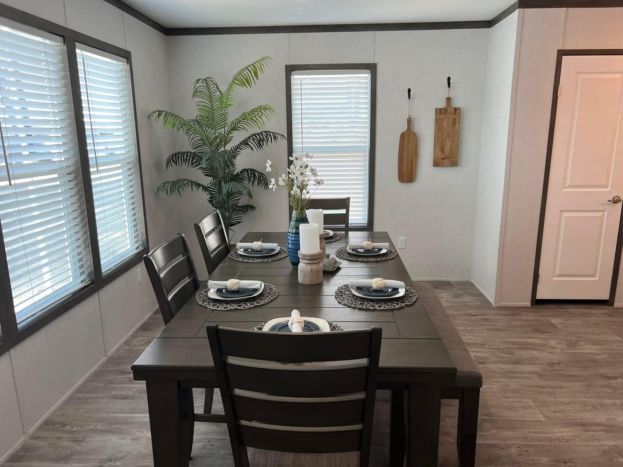 A modern dining room with a dark wooden table set for six, featuring blue plates and white napkins. A potted plant and decor adorn the space.