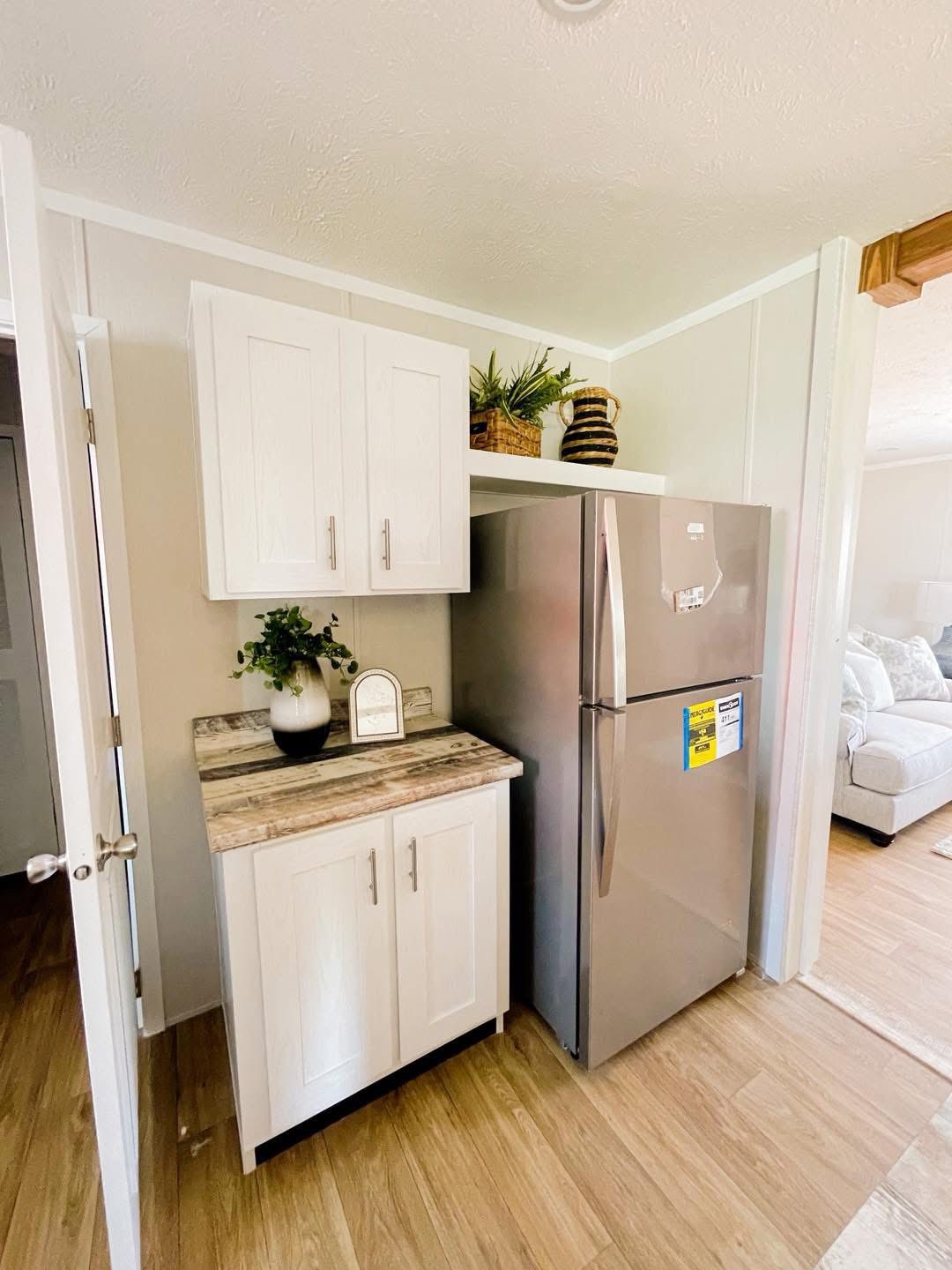Compact kitchen area with a stainless steel fridge, white cabinets, and wooden countertop. Potted plants add a touch of greenery. Cozy and modern tone.