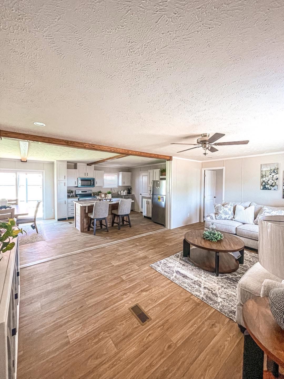 Spacious, modern living area with wooden floor and white walls. Features a cozy lounge with a round table, and an open kitchen with an island and chairs.