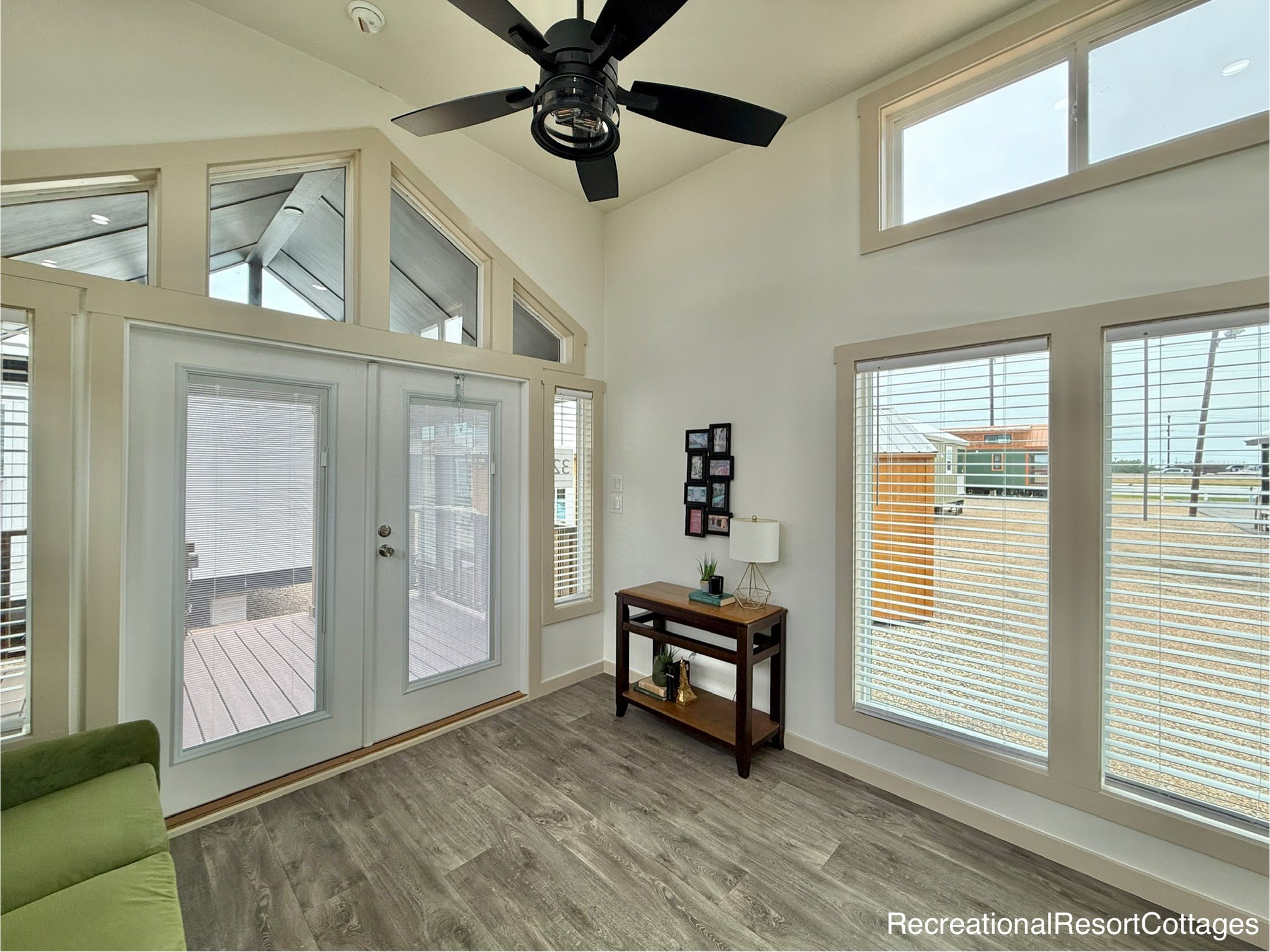 Bright room with large windows and glass doors, featuring a ceiling fan and modern decor. Sunlight fills the space, creating a cozy, welcoming atmosphere.