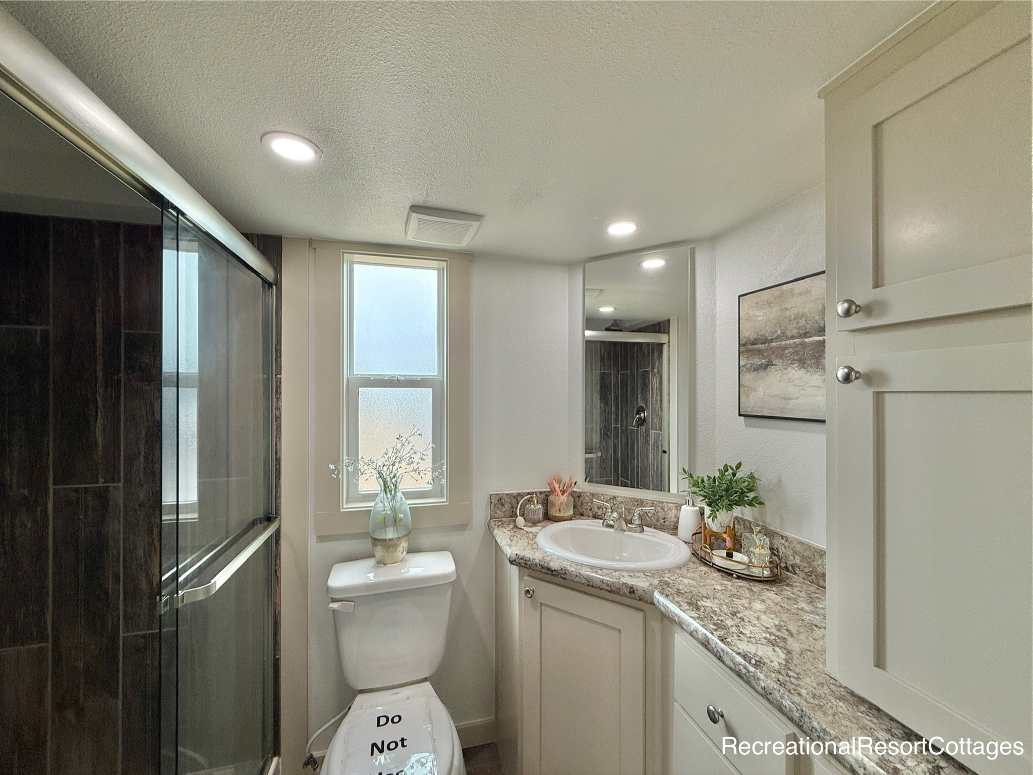 Modern bathroom with a glass shower, marble countertop, and white cabinets. Soft lighting and decor create a clean and welcoming atmosphere.