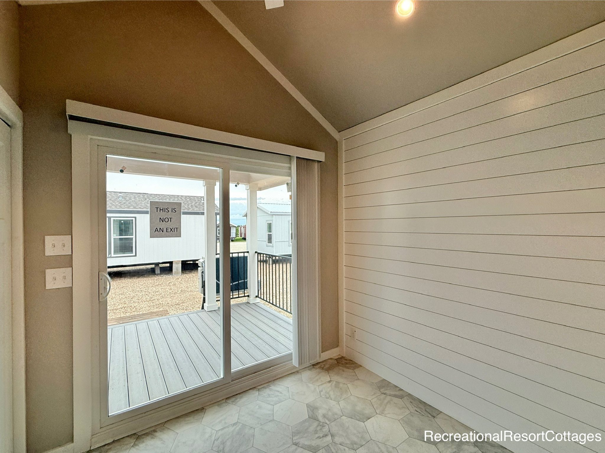 Bright room with gray hexagonal tile flooring and a shiplap wall. A sliding glass door leads to a small porch. A sign reads, "This is not an exit."