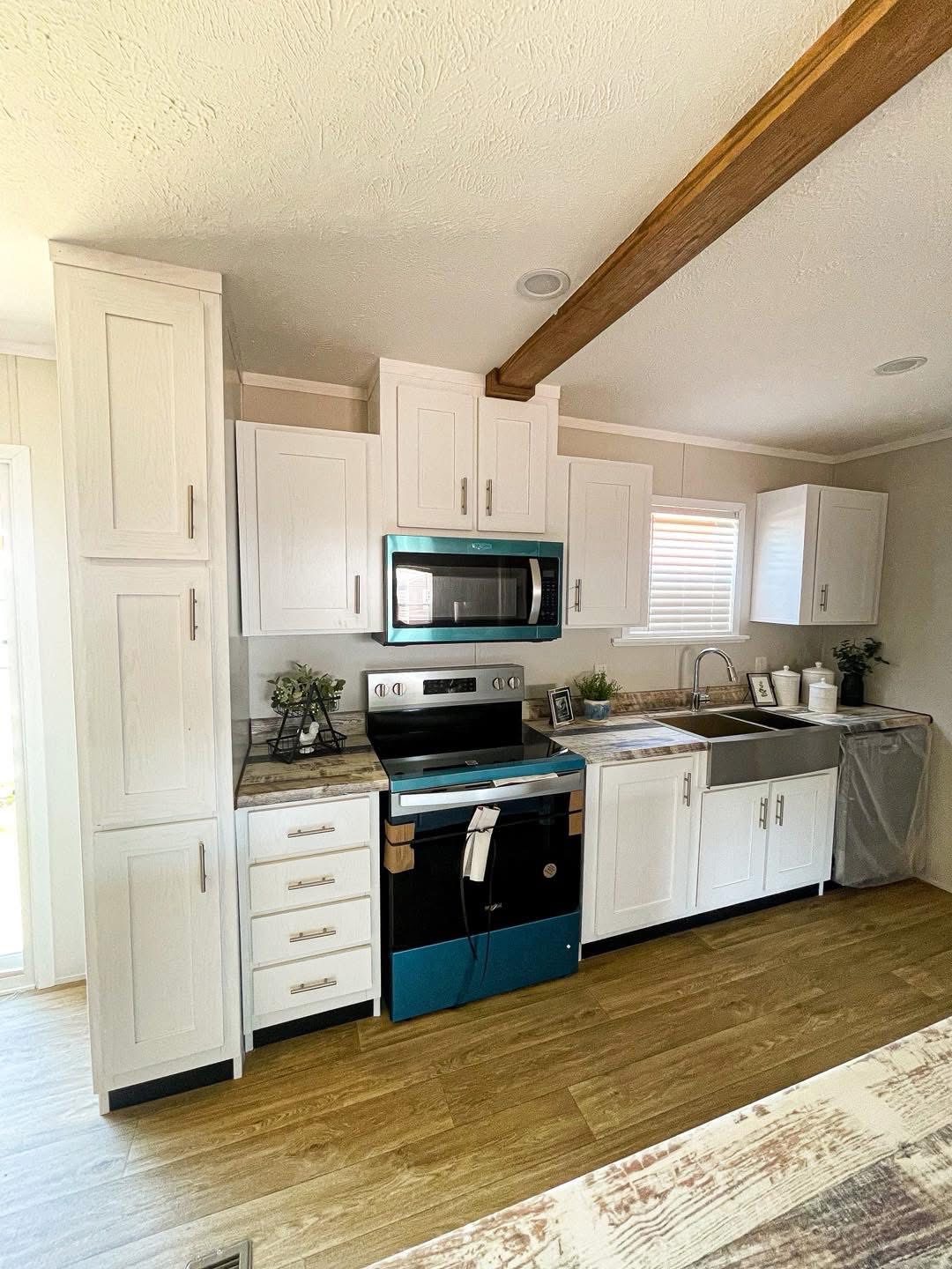 Modern kitchen with white cabinets, stainless steel appliances, and wood accents. A microwave and stove are centered below a wooden ceiling beam.