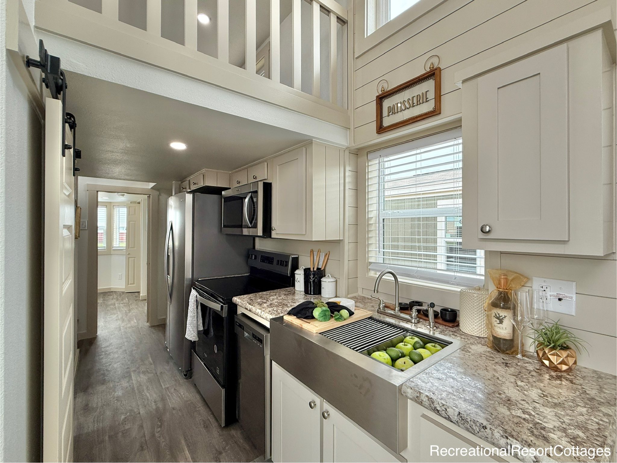 Compact, modern kitchen with white cabinets, granite countertops, and stainless steel appliances. A window above the sink provides natural light.