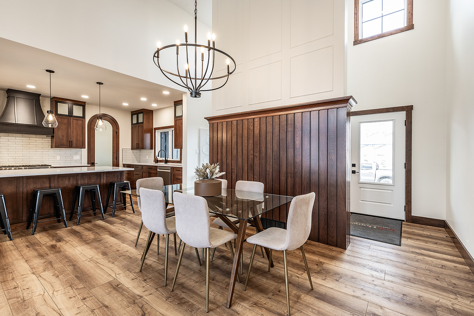 Spacious dining area with glass table, beige chairs, and a modern chandelier. Nearby, a kitchen with wooden cabinets and bar stools exudes a warm, inviting feel.
