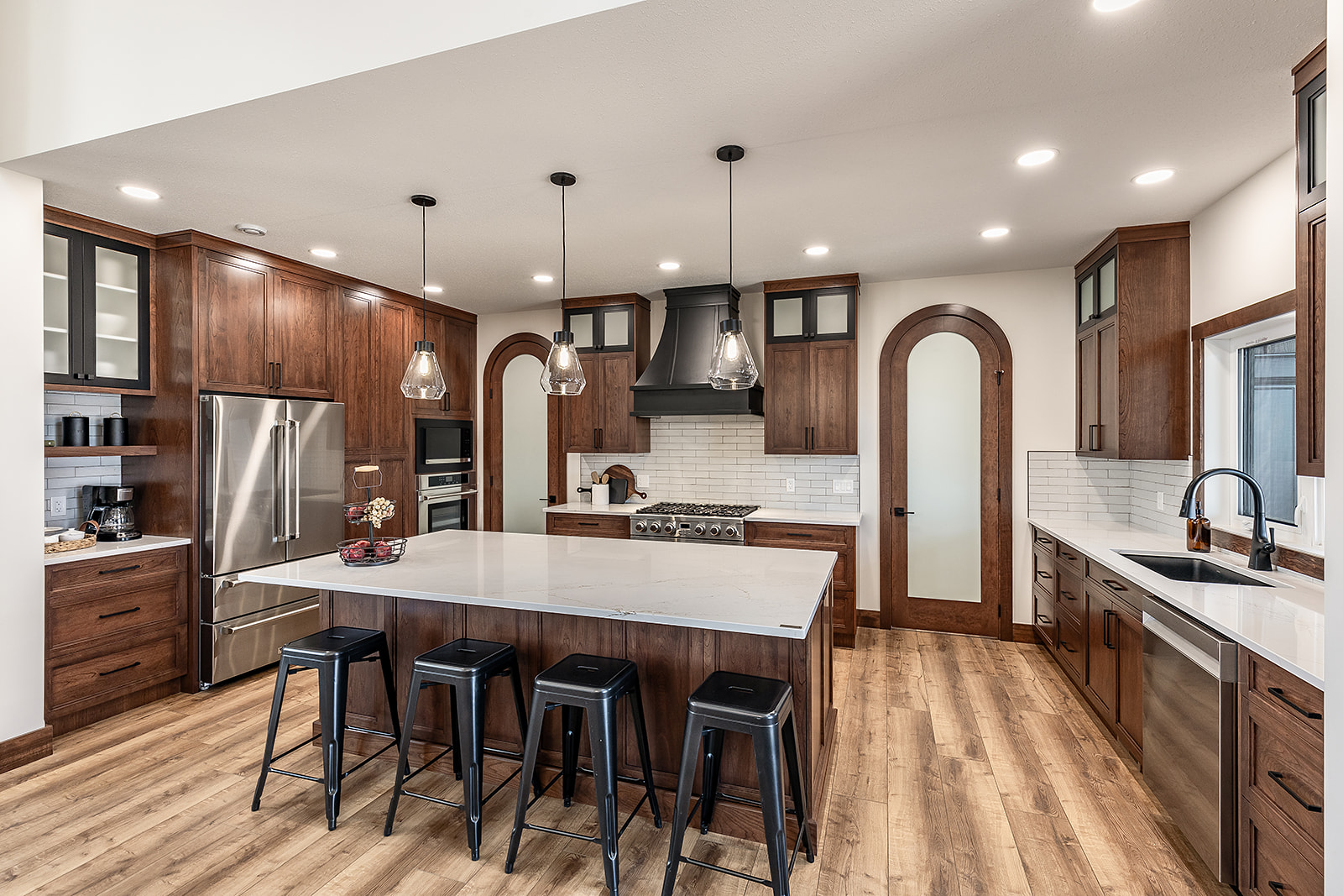Modern kitchen with wooden cabinets, marble island, and stainless steel appliances. Pendant lights hang above, creating a warm, inviting atmosphere.