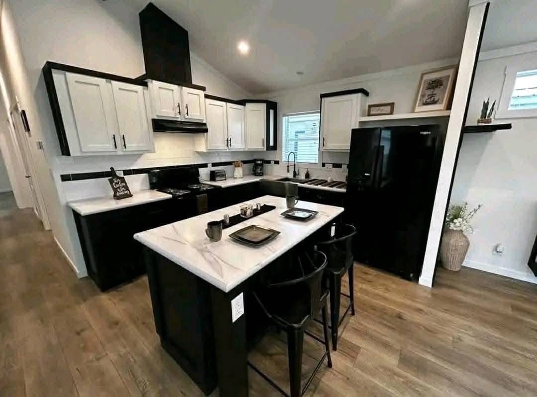 Modern kitchen with white and black cabinets, marble countertops, and wooden flooring. An island features black stools and tableware, creating a sleek, inviting space.
