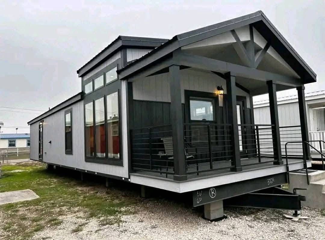Modern tiny house with a black and white exterior, featuring large windows and a covered porch with railing. Overcast sky creates a cozy mood.